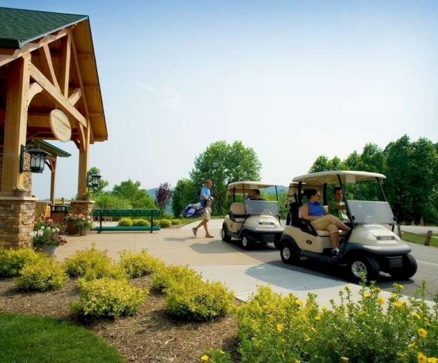 A scene at a golf course entrance shows two golf carts with people inside, a person carrying a bag, and a charming wooden building.