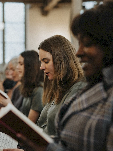 People seated in a church or classroom, reading from hymnals or books during a service or study session.