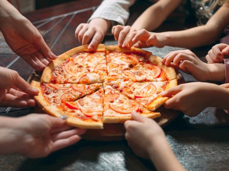 A group of people sharing a pizza, each grabbing a slice together, teamwork and tasty snacks bring everyone closer, delicious moment.