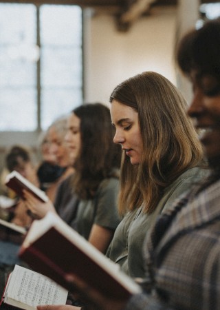 People seated in a church or classroom, reading from hymnals or books, focused on the text as they participate in a service or class.