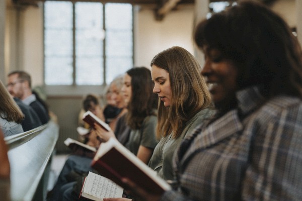 People seated in a church or classroom, reading from hymnals or books, focused on the text as they participate in a service or class.