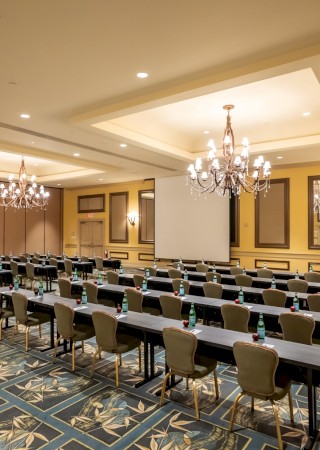 A spacious conference room set for a seminar with long rows of tables and chairs, chandeliers, ornate walls, and patterned carpet, ready for attendees.