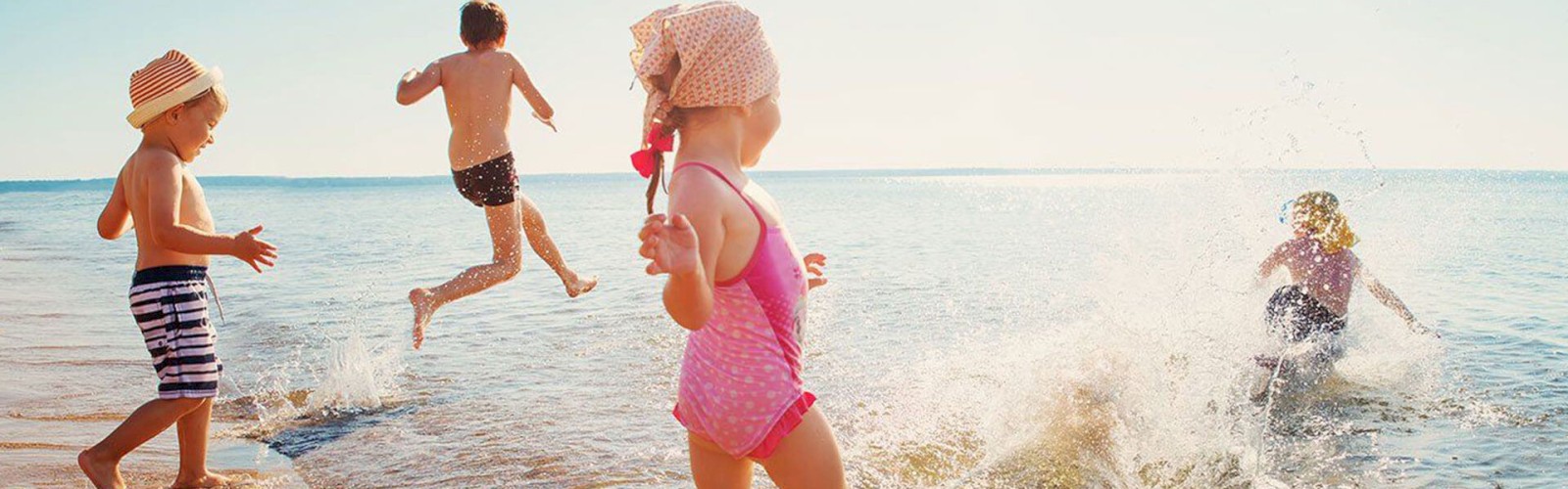 Four children are playing at the beach, splashing water and enjoying the sun, with one child jumping into the water, creating a splash.