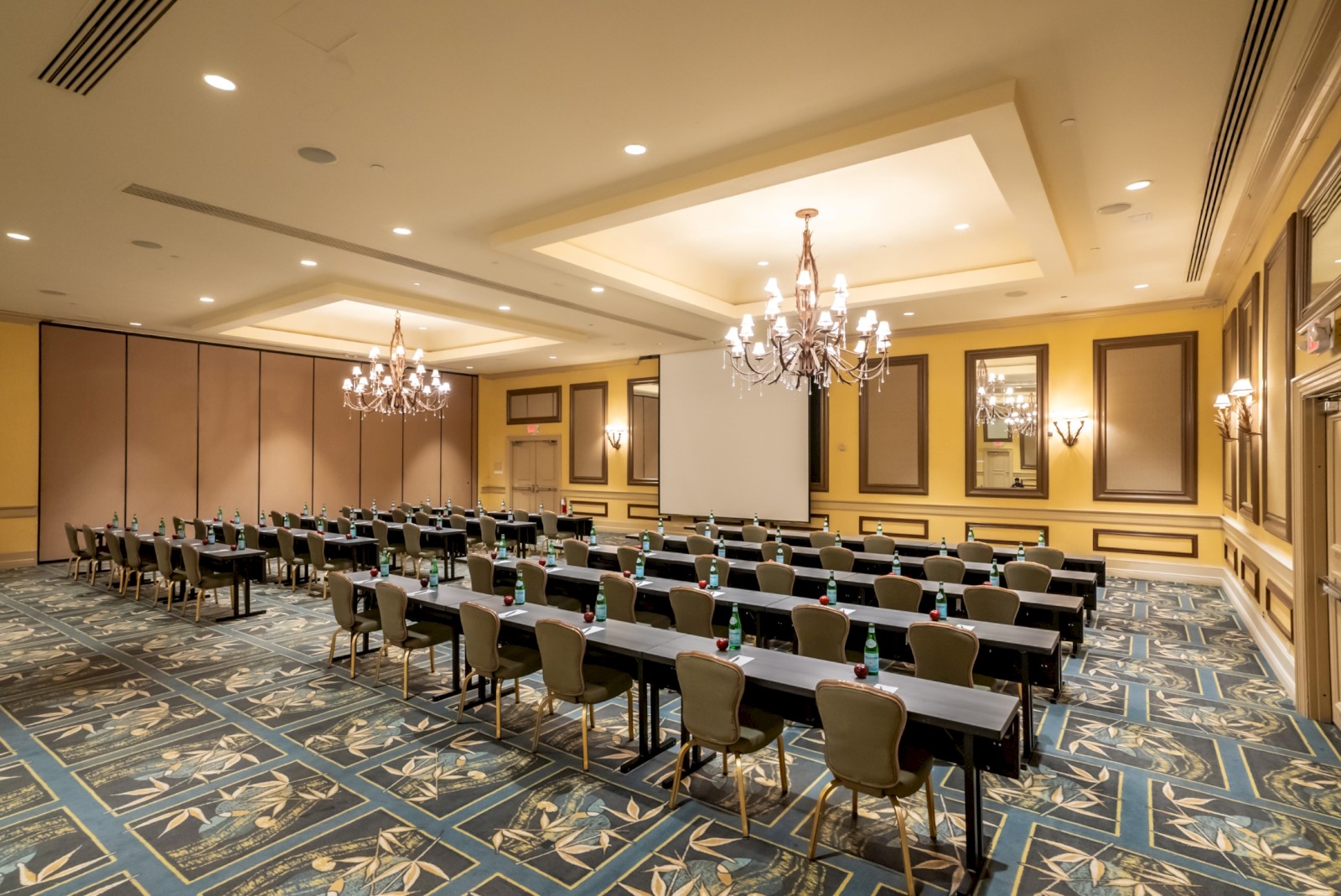 A large conference room set up with long rows of desks and chairs, chandeliers, and ornate wood paneling for a formal meeting.