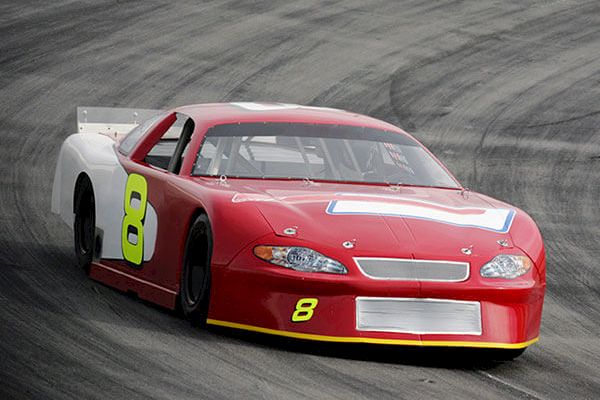 A red race car with the number 8, featuring a white roof design and driving on a racetrack corner, is shown. The car has a sleek design.