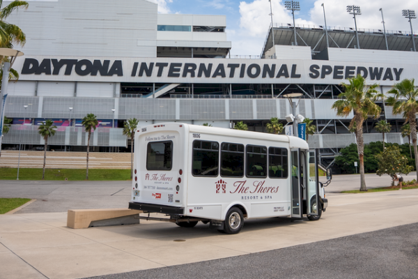 A shuttle bus is parked outside Daytona International Speedway on a sunny day with a partly cloudy sky.