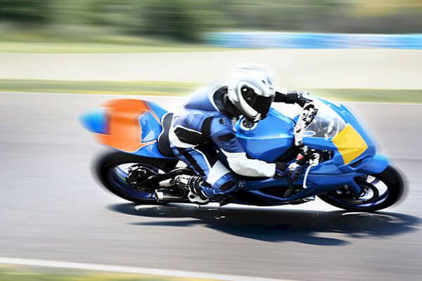 A person wearing protective gear is riding a blue motorcycle at high speed on a racetrack, with a blurred background indicating motion.