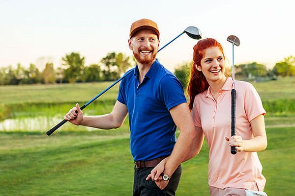 A man and a woman are smiling while holding golf clubs on a green golf course. They appear to be enjoying their time together outdoors.
