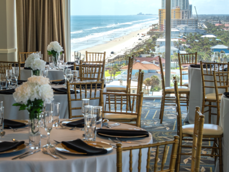 Elegant banquet setup with white tablecloths, black napkins, gold chairs, and a stunning ocean view.