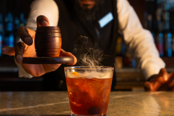 A bartender garnishes a steaming cocktail at a dimly lit bar, creating an inviting and mysterious atmosphere for patrons.