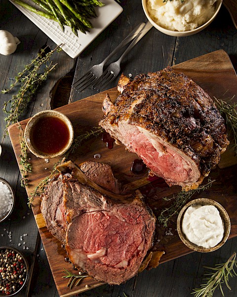 A perfectly roasted beef loin, sliced to reveal a juicy pink center, served with sauces and fresh herbs on a rustic board.