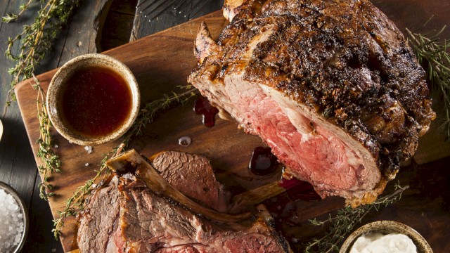 A perfectly roasted beef loin, sliced to reveal a juicy pink center, served with sauces and fresh herbs on a rustic board.