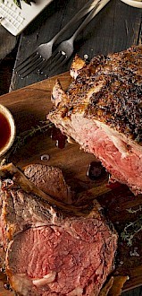 A perfectly cooked, juicy roast beef steak on a wooden cutting board with sides of dipping sauces and a glass of red wine.