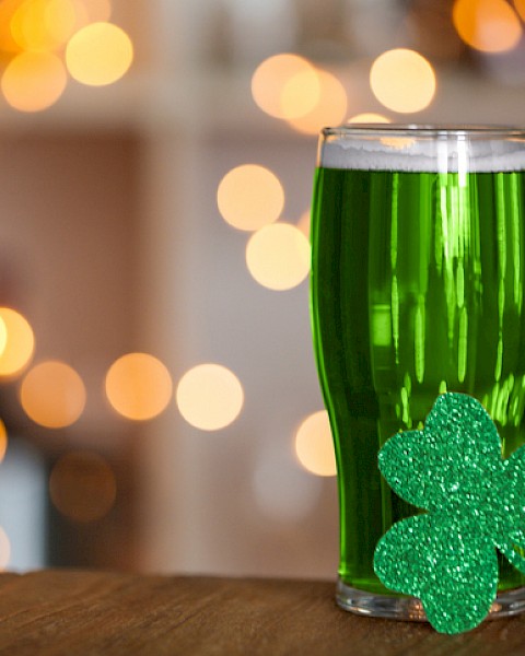 A glass of green beverage decorated with a glittery shamrock, set against a festive, bokeh-lit background for St. Patrick's Day.