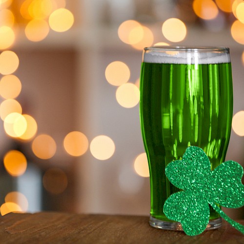 A glass of green beverage decorated with a glittery shamrock, set against a festive, bokeh-lit background for St. Patrick's Day.