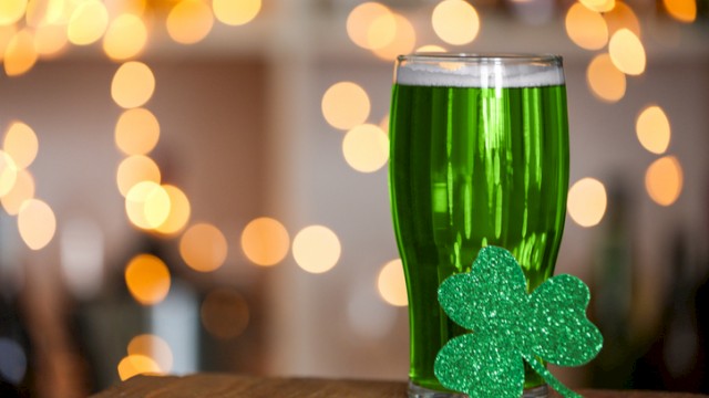A glass of green beverage decorated with a glittery shamrock, set against a festive, bokeh-lit background for St. Patrick's Day.