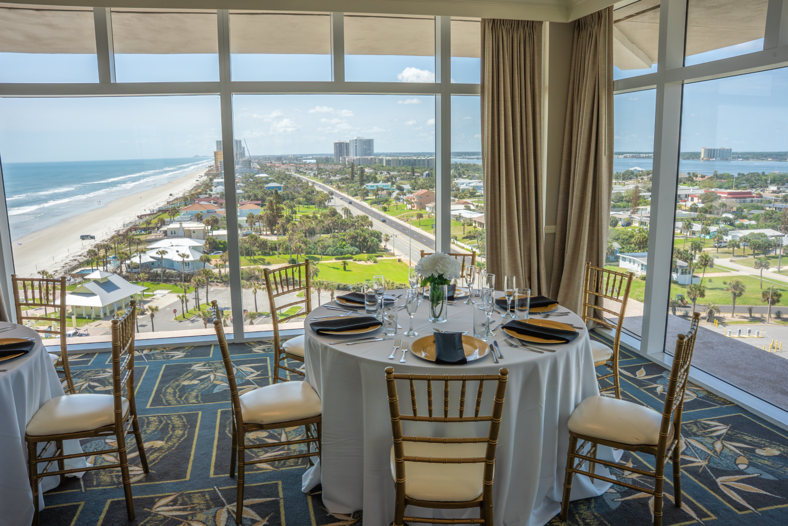 Around a dining table with black and gold settings, overlooking a beach and cityscape through large windows.