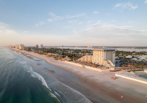 An aerial view of a beachside city with buildings, a sandy shore, and calm ocean waves during sunset.