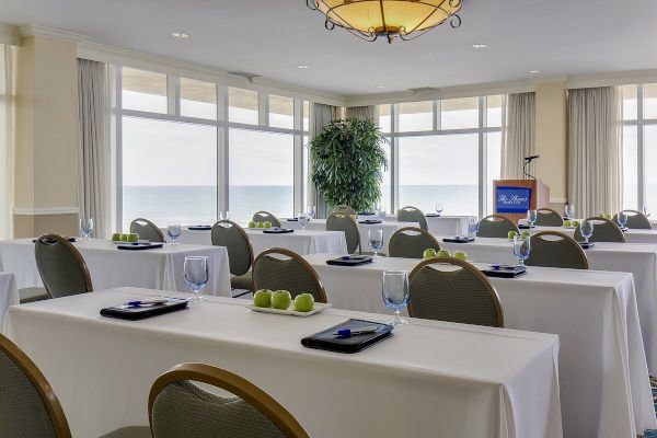 A conference room setup with tables, chairs, notepads, and apples on each table, large windows with an ocean view, and a podium at the front.