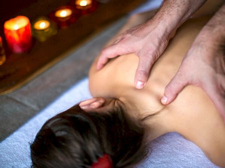 A person is receiving a back massage on a towel, with lit candles placed nearby for a relaxing ambiance.