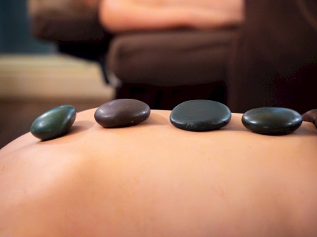 Two people are receiving hot stone massages, with smooth stones placed on their backs for relaxation.