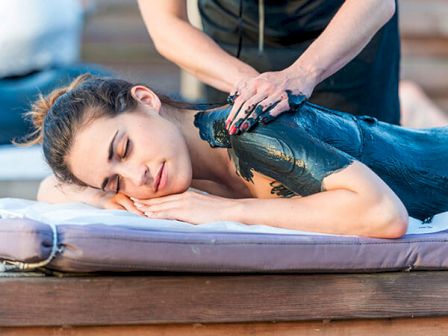 A woman is receiving a relaxing mud massage while lying on a massage bed outdoors, ending the sentence.