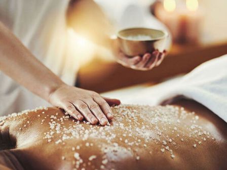 A person is getting a relaxing massage with salt being applied to their back. The scene is calm and serene, suggesting a spa environment.
