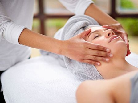 A person is receiving a facial massage, lying down with a towel wrapped around their head, showing a relaxed and serene expression.