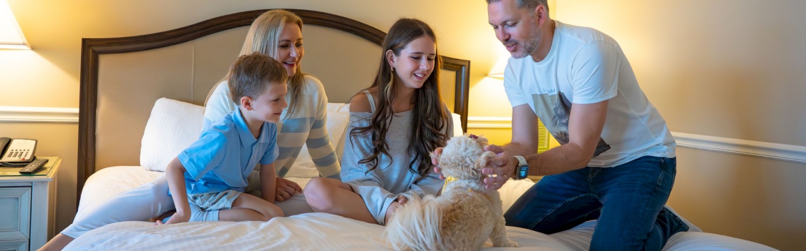A family is sitting on a bed playing with a small dog, creating a warm and joyful scene in the room.