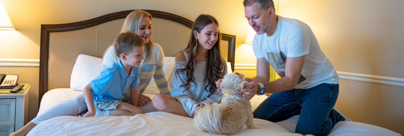 A family is sitting on a bed playing with a small dog, creating a warm and joyful scene in the room.