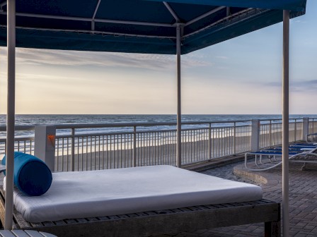 A tranquil beach view from a shaded cabana with loungers and a calm sea