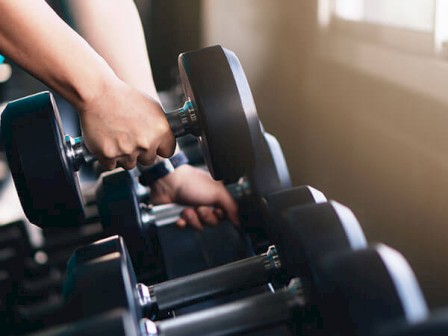 Close-up of hands picking a dumbbell from a rack at the gym.