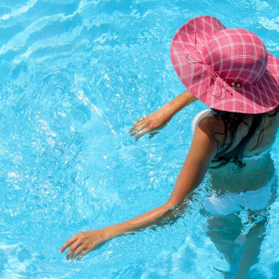 A person wearing a red hat and white swimsuit is standing in a swimming pool with clear blue water.