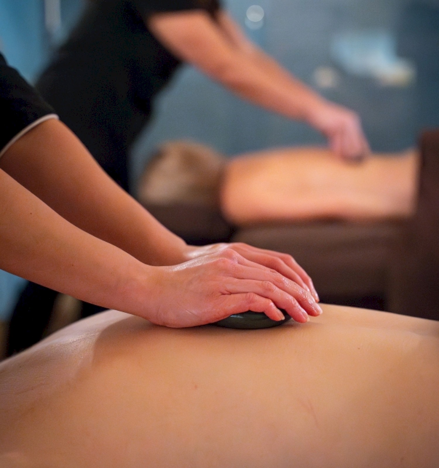 People receiving massages at a spa, with one person applying pressure on a person's back.