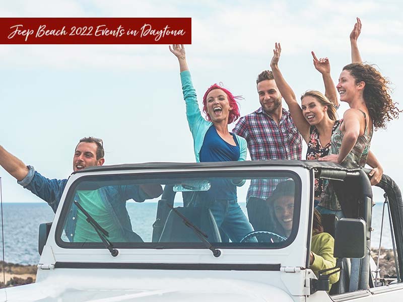 A group of people is standing in a white Jeep with their arms raised, next to the ocean. The photo reads 