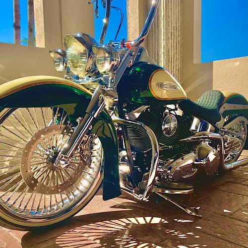 The image shows a shiny custom motorcycle with chrome detailing and unique features, parked indoors with sunlight casting shadows.