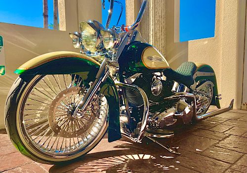 The image shows a shiny custom motorcycle with chrome detailing and unique features, parked indoors with sunlight casting shadows.