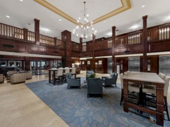 This image shows a spacious hotel lobby with elegant wooden railings, a chandelier, seating areas, and elevators.