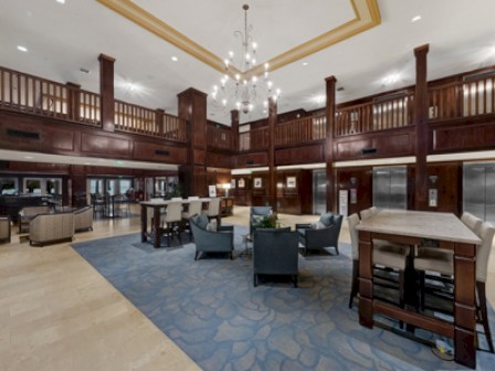 This image shows a spacious hotel lobby with elegant wooden railings, a chandelier, seating areas, and elevators.