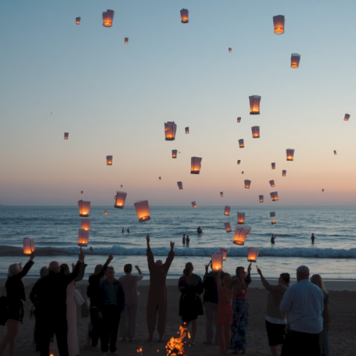 People release floating lanterns into the sky at sunset on a beach celebration.