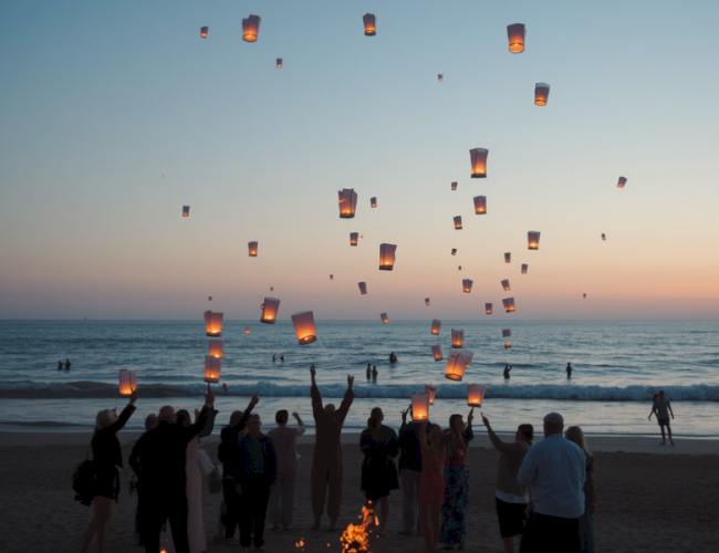 People release floating lanterns into the sky at sunset on a beach celebration.