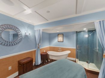 A cozy bathroom with a standalone bathtub, a glass shower, blue walls, and elegant lighting with a large circular mirror on the side wall.