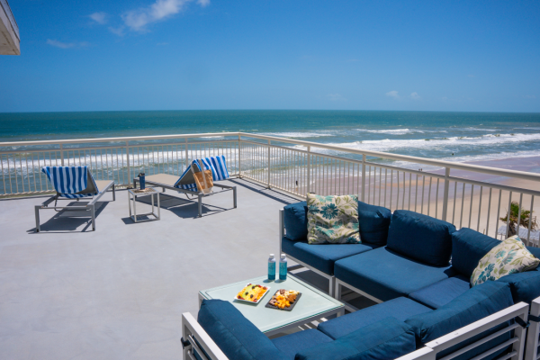A balcony with blue seating, umbrellas, and ocean views during sunny weather.