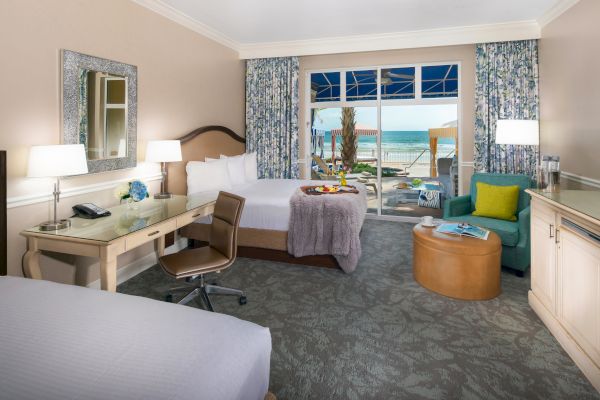 A hotel room with two beds, a desk, a chair, a seating area, and a view of the ocean through a glass door, ending the sentence.