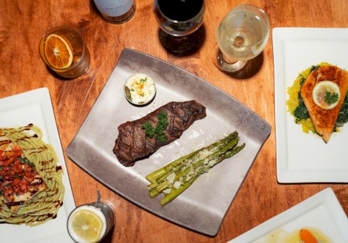 A meal with steak, asparagus, and sauces, alongside wine, lemon water, and a dessert shot on a wooden table.