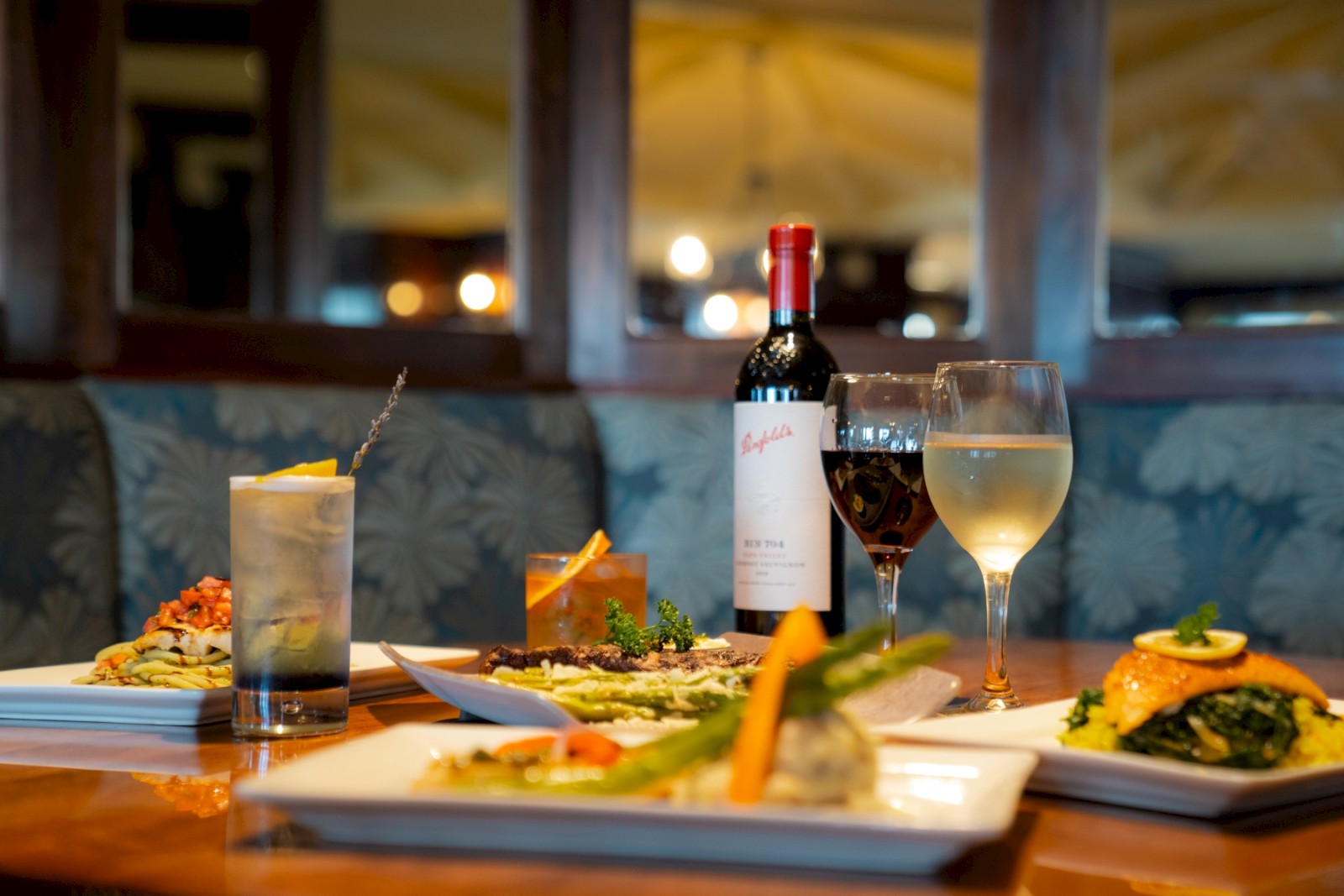 A dinner table set with wine, cocktails, and plated dishes in a cozy restaurant ambiance.