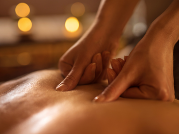 The image shows someone receiving a back massage with candles glowing in the background, suggesting a relaxed, serene atmosphere.