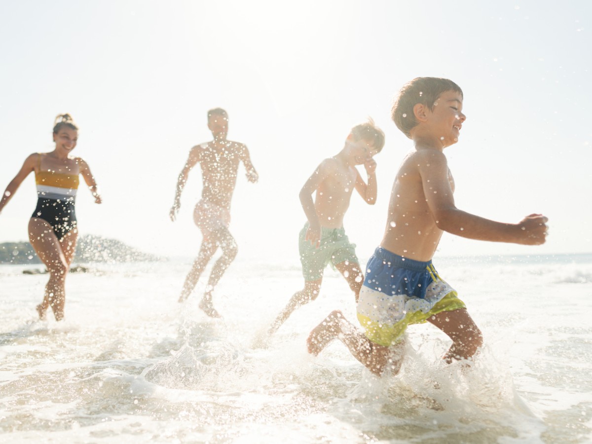A family is running and playing in the shallow water at the beach on a sunny day, enjoying the waves and the pleasant weather, ending the sentence.
