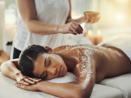 A woman receives a salt scrub massage in a relaxing spa setting with a therapist applying treatment on her back.