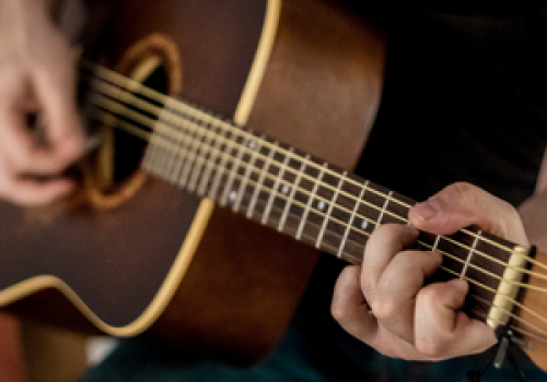 Someone is playing an acoustic guitar, focusing on their hands and the strings for a close-up view of the musical performance.